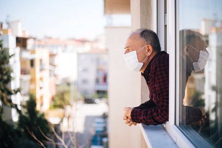 Senior man in medical mask on window breathing fresh air from quarantine